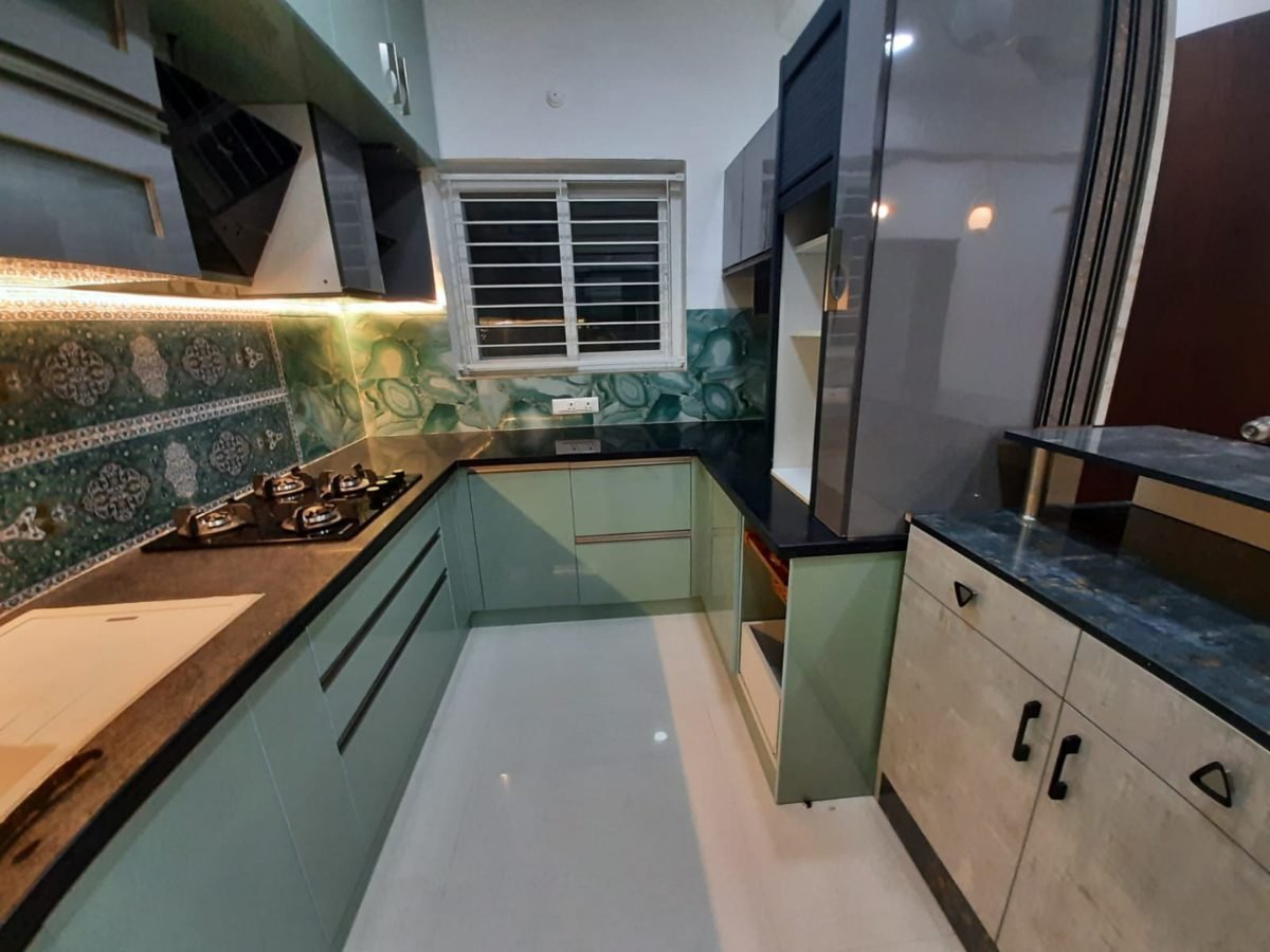 L-shaped modular kitchen in glossy sea green with granite counter and tall unit